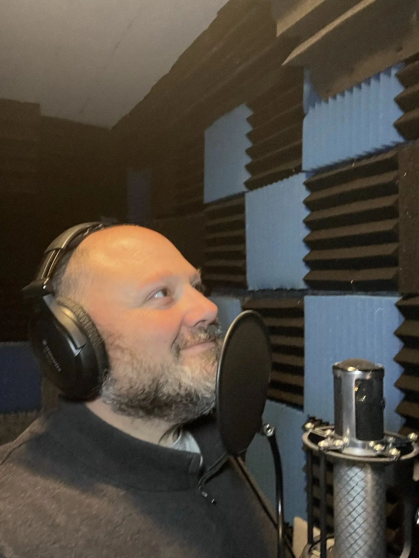 Anthony Pica at the microphone in his booth, wearing headphones and looking up mid-read